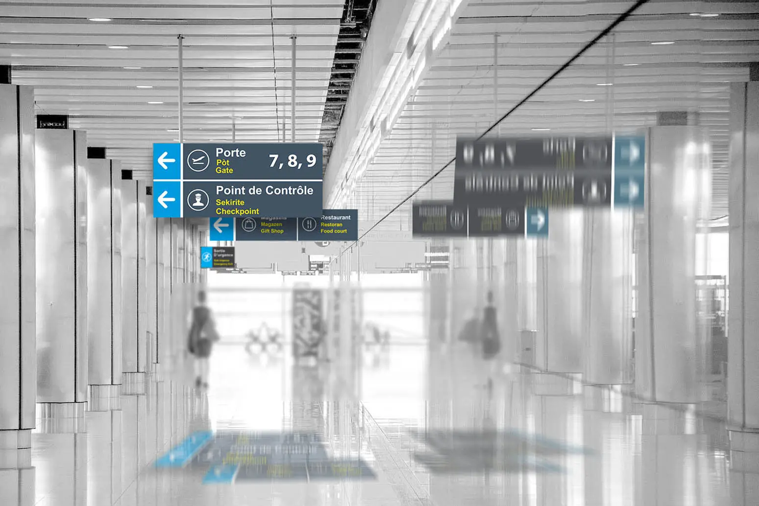 Airport corridor with blue trilingual overhead signs pointing to the gates and security.
